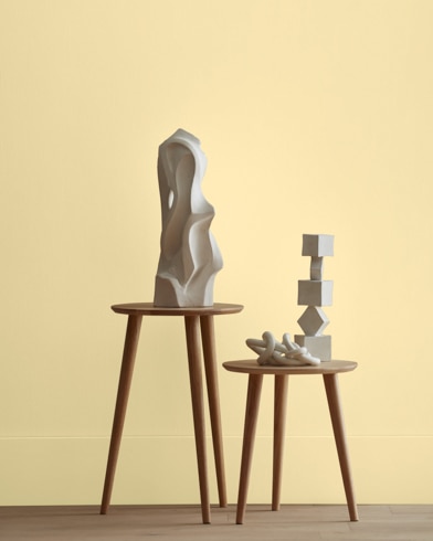 White abstract scupltures stand on wooden stools in front of a wall painted Popcorn Kernel.