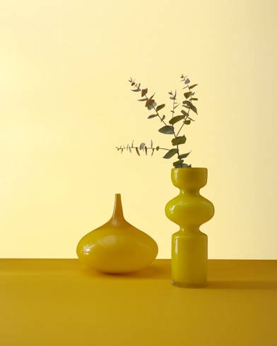Two abstract ceramic potters, one with a plant, sit in front of a wall painted Hay Stack.